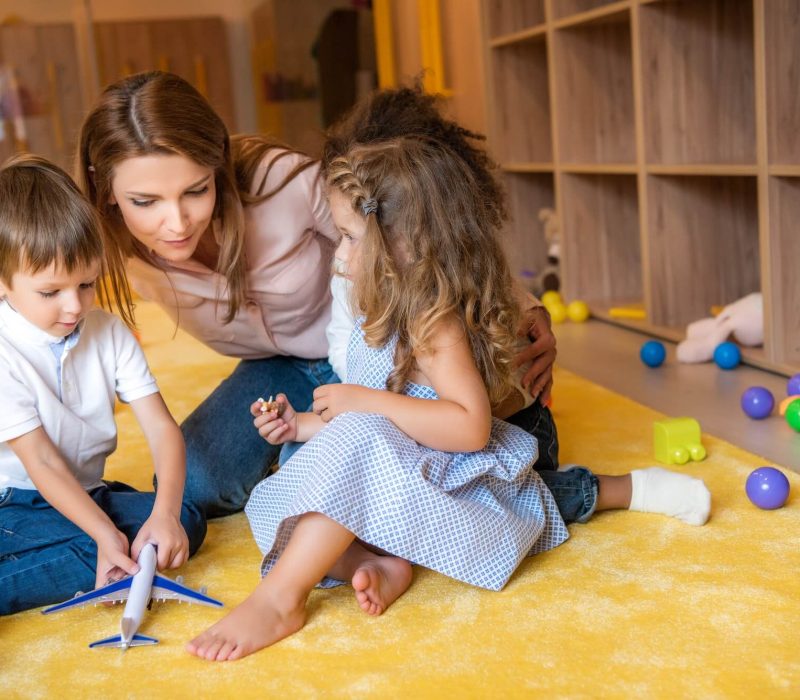 tutor-hugging-adorable-kids-on-carpet-in-kindergarten-1.jpg